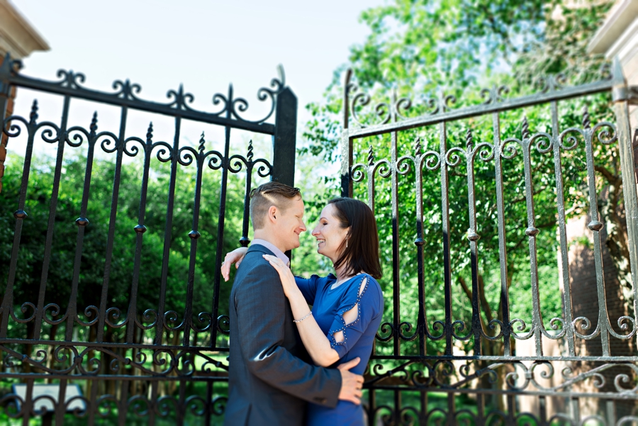 A man holds his girlfriend in front of iron gates.